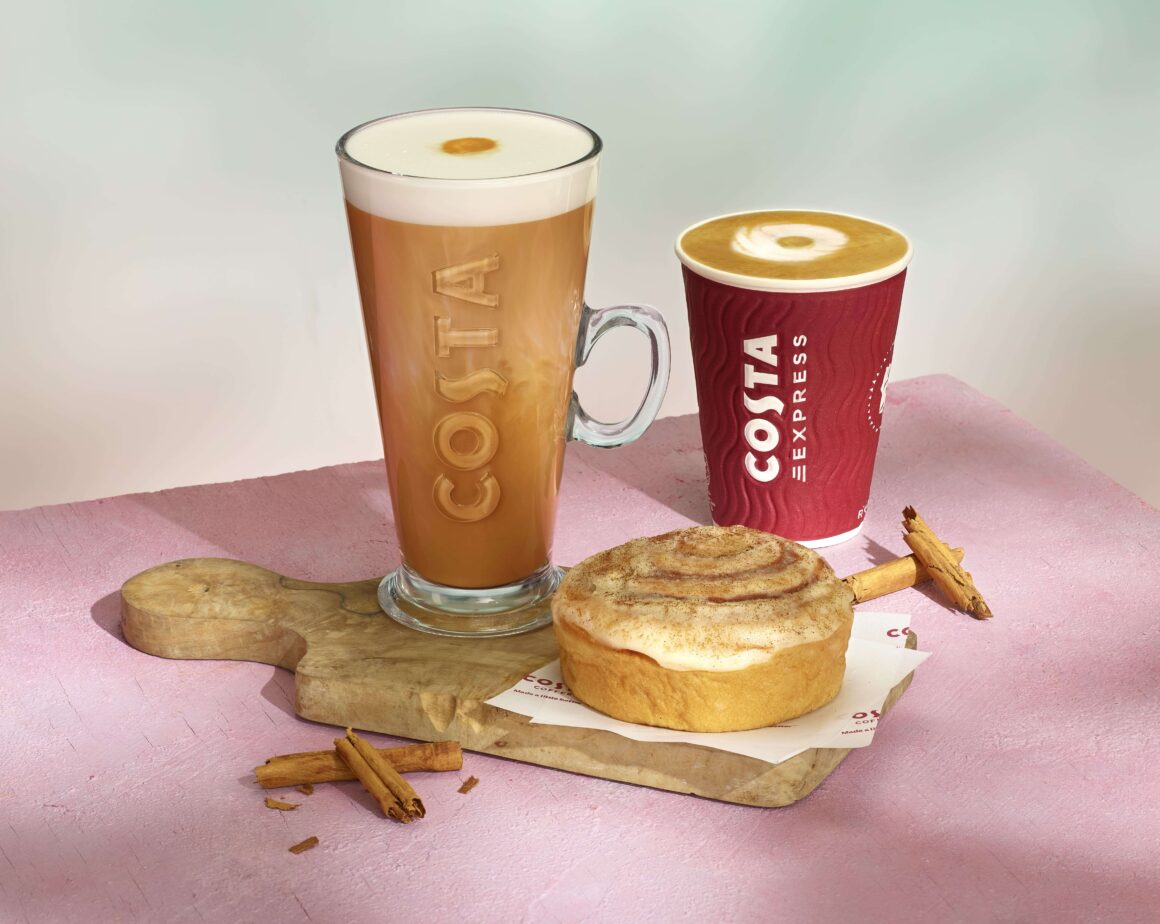 Cinnamon bun lattes from Costa in a glass Costa mug and a takeaway cup behind a cinnamon bun.
