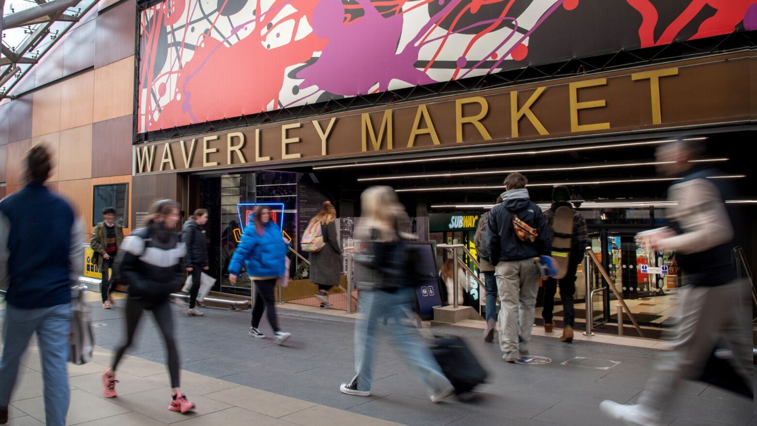 An image of blurry people walking past the entrance to Waverley Market