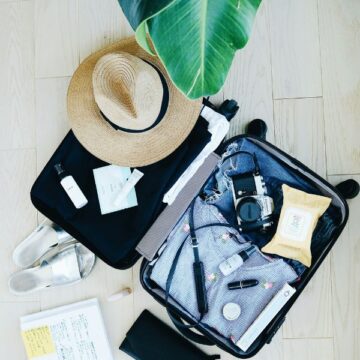 suitacse_600x600 A suitcase full of clothes and toiletries with a sun hat on top