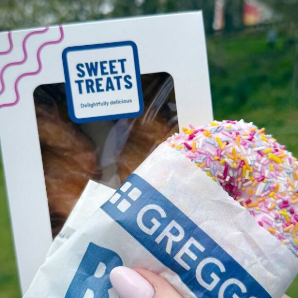 Greggs doughnut with pink sprinkles held against a sweet treats box